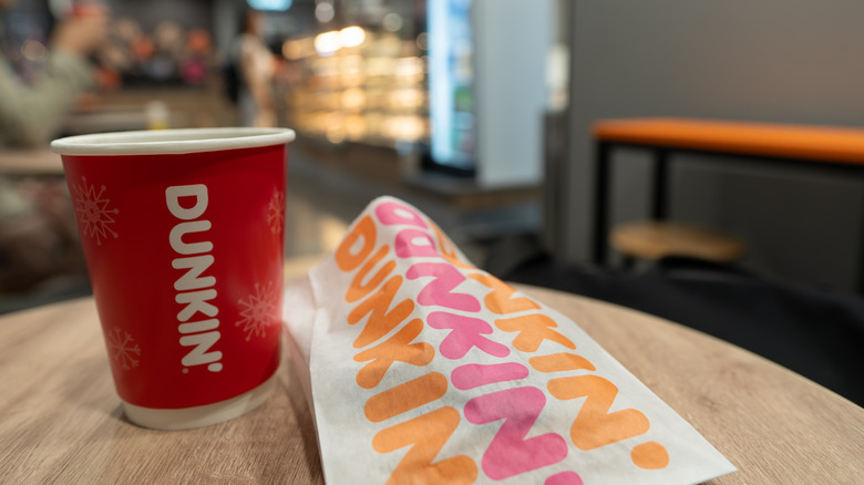 Dunkin' branded coffee and food wrapper on table, blurred background.