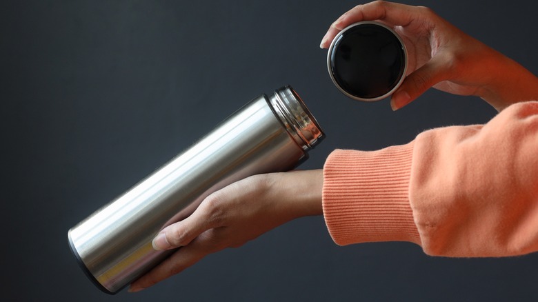 Woman holding opened thermos and lid with dark background