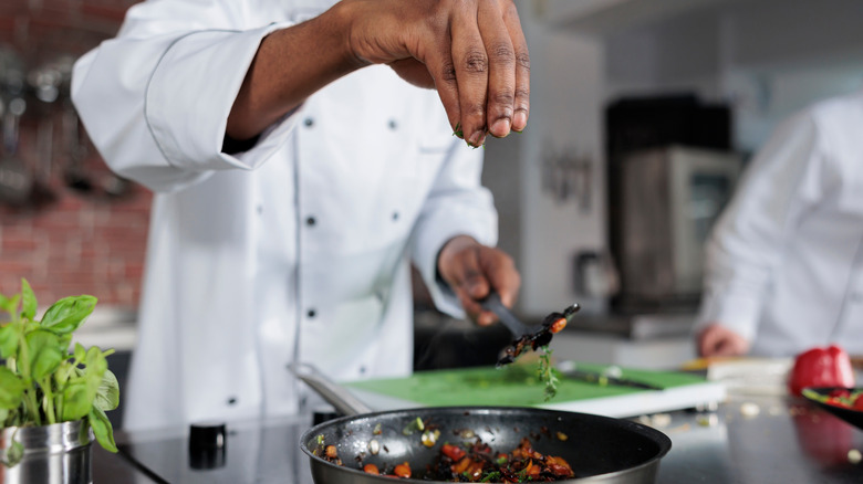 A chef seasoning food in a pan