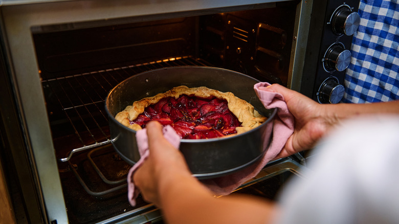 A person removing a dessert from the oven with a towel