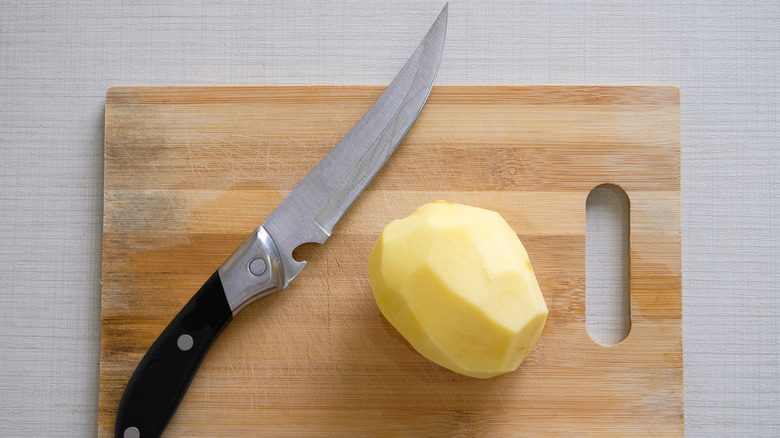 A potato and a knife on a wooden cutting board