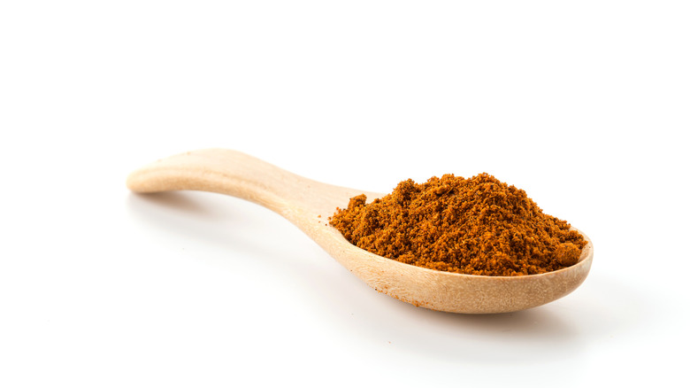 Orange-brown regular paprika sits heaped atop a wooden spoon on a white background