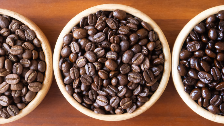 A close-up of a pot of medium roast coffee beans, with light and dark roast on either side, on a wooden surface