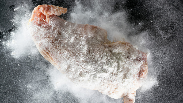 a chicken breast covered in flour on a black surface