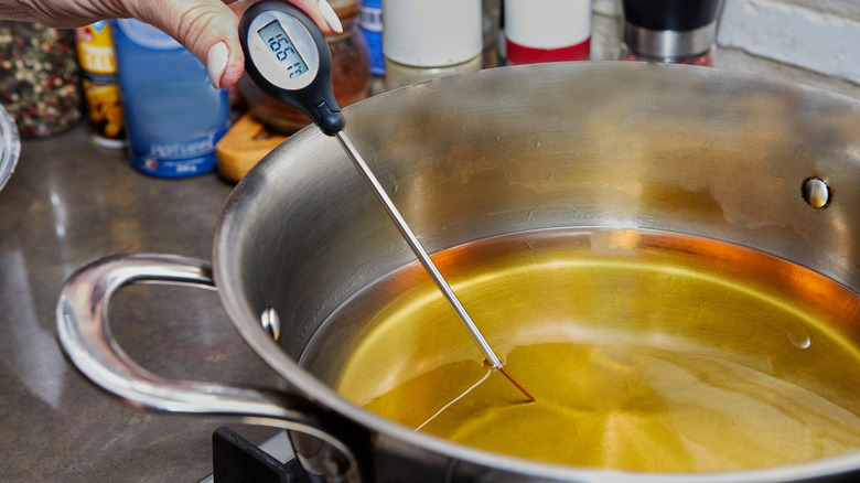 Chef checks the temperature of the heated oil in pot on gas stove with thermometer