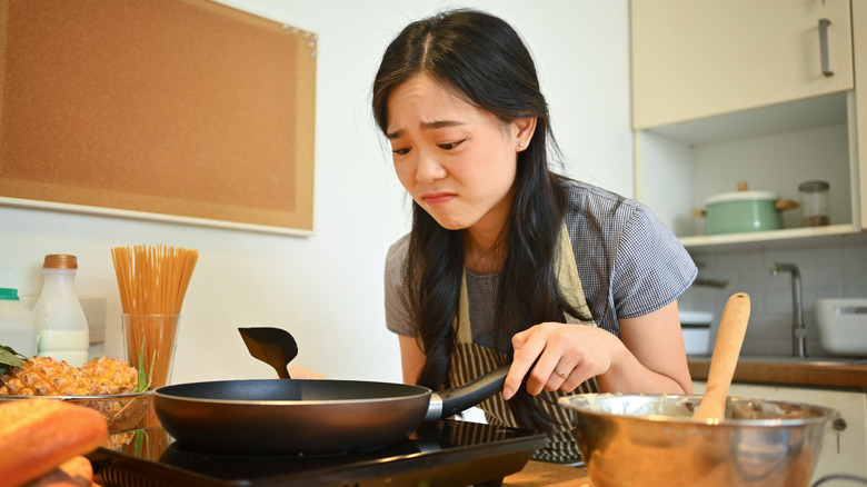 Unhappy woman looking in a frying pan with worried face expression