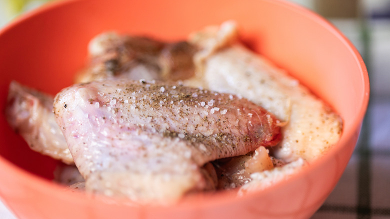 Close up of chicken wings in a red bowl sprinkled with coarse salt and black pepper