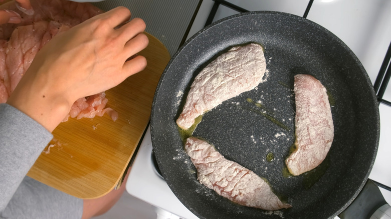 woman frying breaded chicken breast in flour on skillet