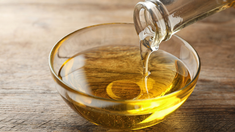 Pouring cooking oil from jug into bowl on wooden table