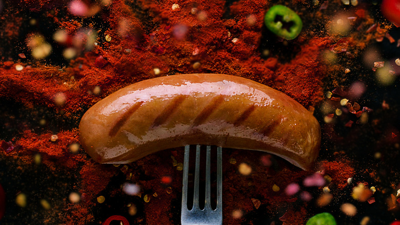 A sausage on a fork, surrounded by an explosion of pepper dust and chillies