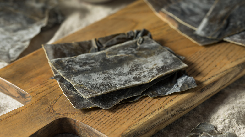 Dried kombu kelp seaweed on wood cutting board.