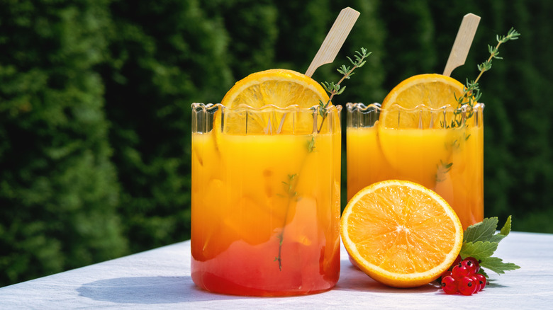 Two glasses of a bright, layered summer cocktail with oranges.