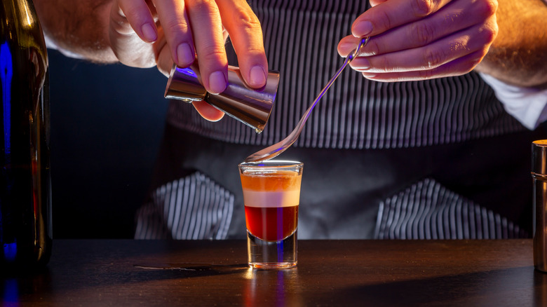 Bartender pouring Irish Cream into a shot using a cocktail spoon.