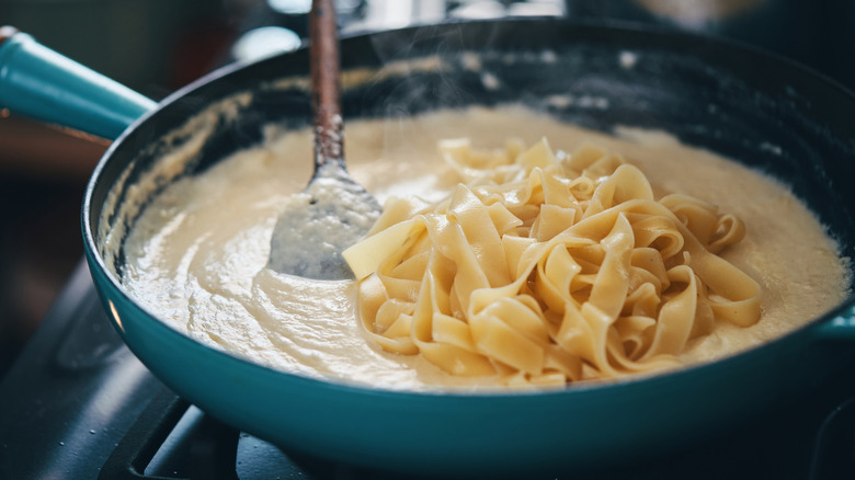 Spatula mixing long noodles and creamy sauce in pan