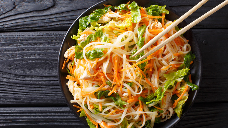 bowl of thin noodles and raw vegetables with chopsticks