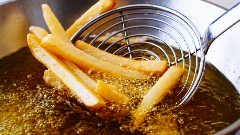 removing french fries from oil with a handheld metal strainer