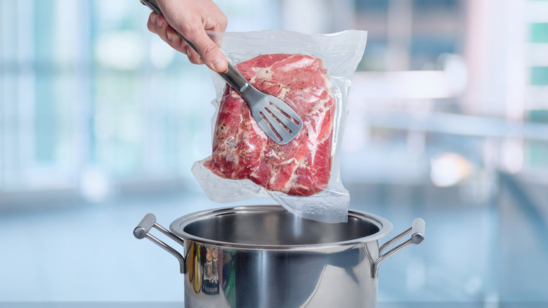 Traditional sous vide being lowered into a pot with tongs