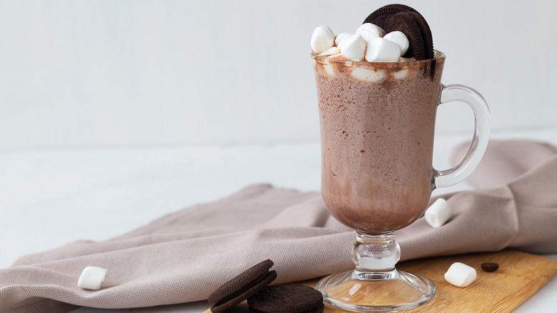 Glass of hot chocolate topped with whipped cream, marshmallows, and cookies.