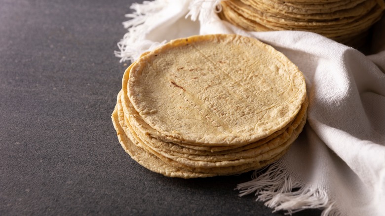 Stack of corn tortillas on dark countertop with white cloth to the side.