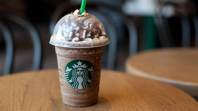 Starbucks Frappuccino in plastic logo cup on round wood table.