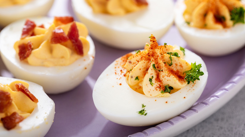 Deviled egg with spices on top, bacon topped deviled eggs in background