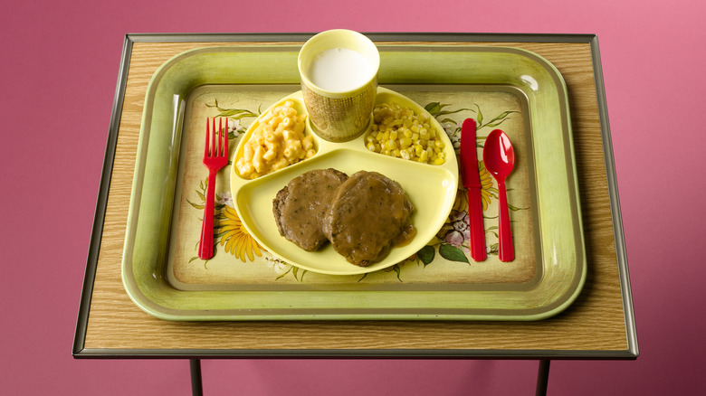 TV dinner with plastic silverware on floral tray atop a foldable table