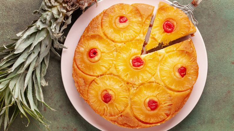 Pineapple upside down cake served on white plate, with one slice being cut out of it