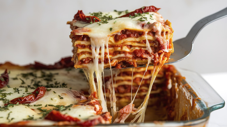 A dish of lasagna with a slice being removed from a baking tray