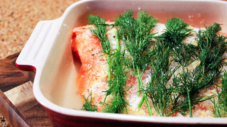 Gravlax brining in a pan with sprigs of fresh dill on top.