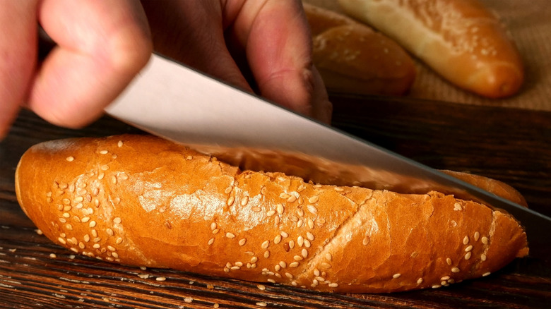 A knife cutting a sesame seed hot dog bun