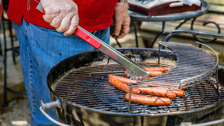 A person turning hot dogs as they cook