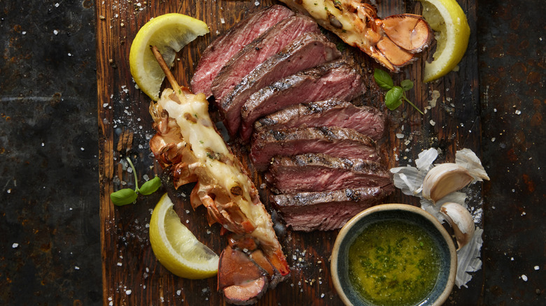 skewered grilled lobster tails and sliced steak on a wood cutting board