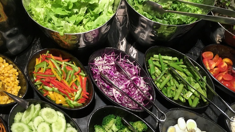 Vegetables and lettuce in pans on a salad bar