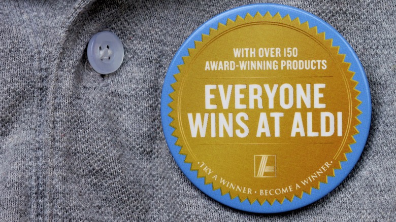 Person wearing badge that reads "Everyone Wins At Aldi" on grey shirt