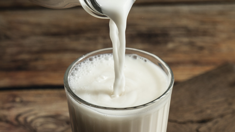 Cream or milk being poured into a glass up to the top on a wood table.