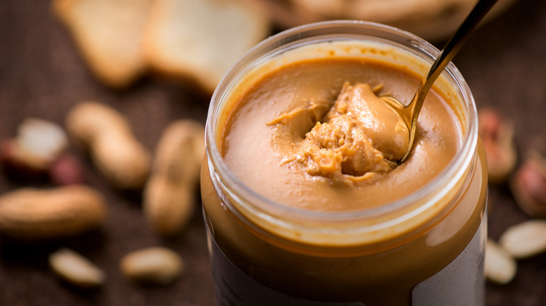 Scooping a spoonful of smooth peanut butter from a jar.