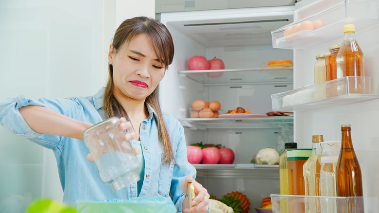 A woman frowning as she cleans out refrigerator.