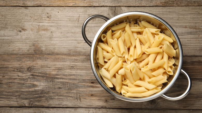 Cooked penne pasta in a strainer on wooden table