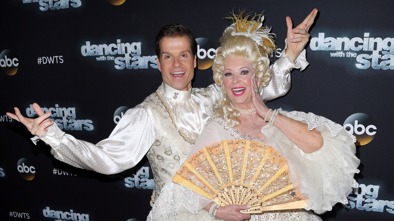 Paula Deen and Louis van Amstel wearing 18th century costumes and posing in front of a Dancing with the Stars banner