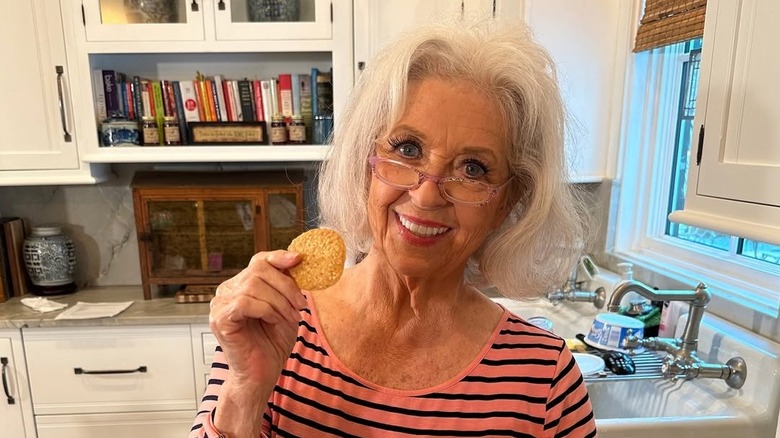 Paula Deen standing in a kitchen and holding up a cookie