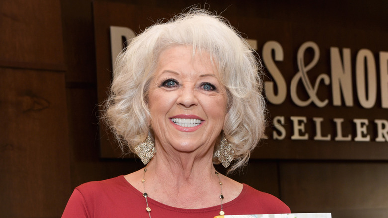 Paula Deen wearing a red top standing in front of a sign for Barnes & Noble