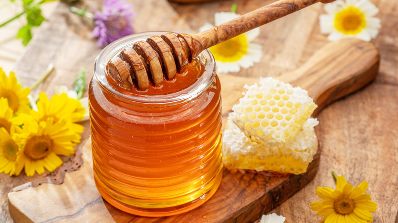 Honey in glass jar with flowers and honeycomb on side