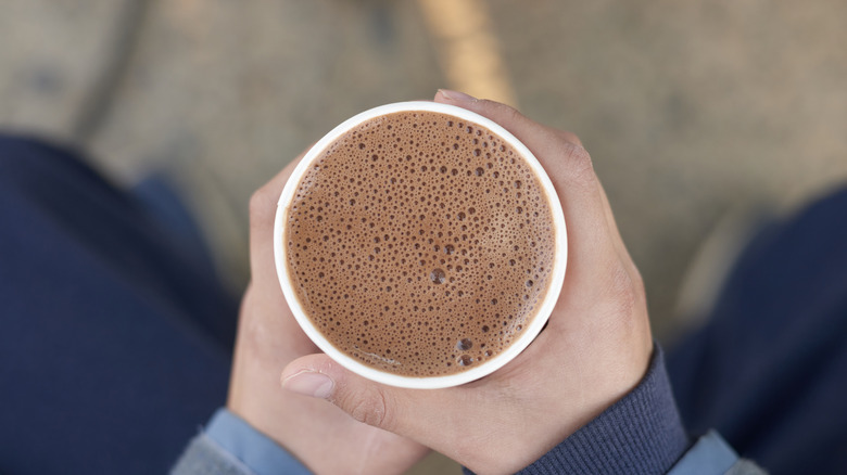 Hands cradle a disposable cup of hot chocolate or cocoa