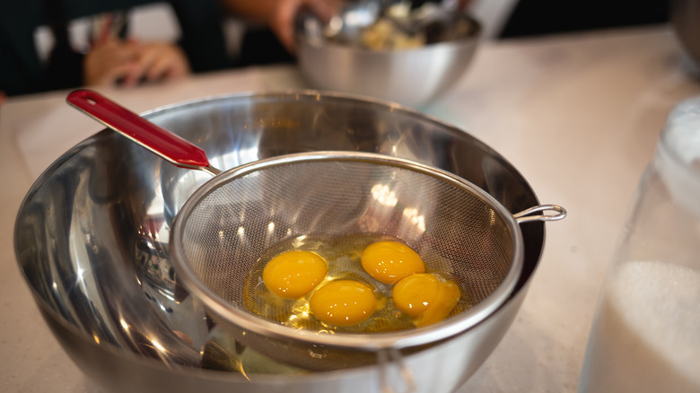 Raw eggs on a sieve resting over a bowl