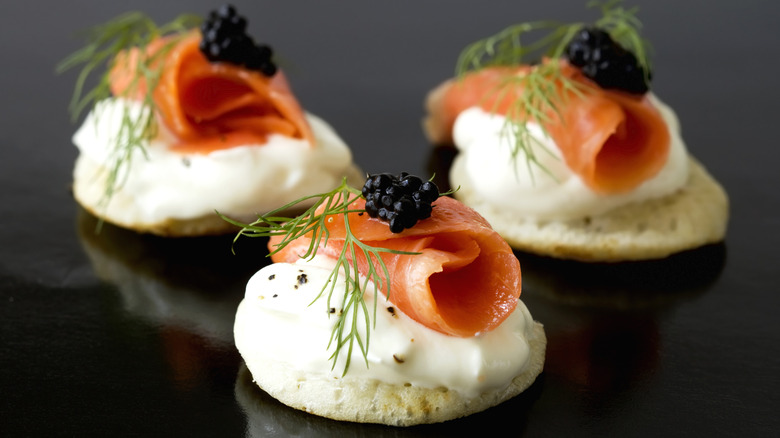 Blini topped with sour cream, salmon, caviar, and fresh dill