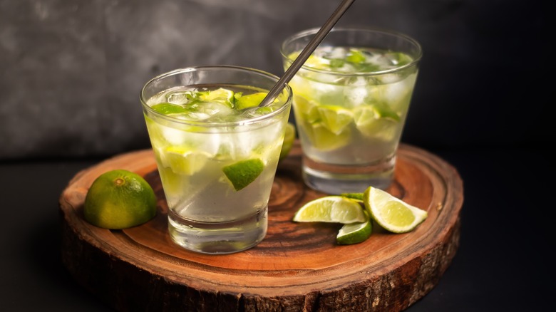 Two caipirinhas with lime wedges on wood table