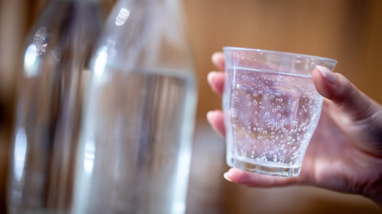 A hand holds a small glass of club soda