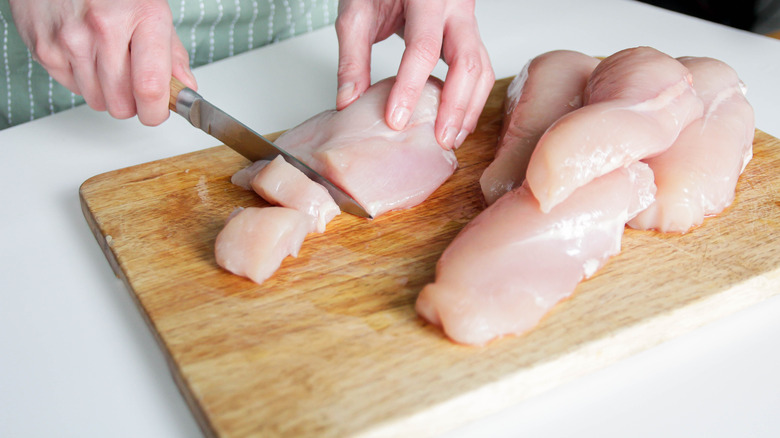 Chopping raw chicken on wood cutting board.