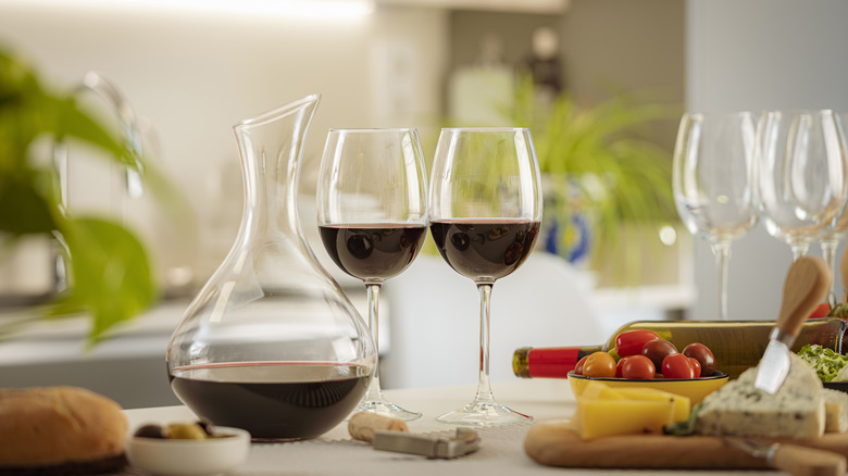 A decanter and two wine glasses filled with red wine.