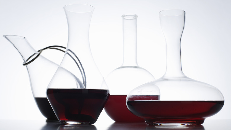 Four differently-shaped wine decanters containing red wine, displayed against bright white background.